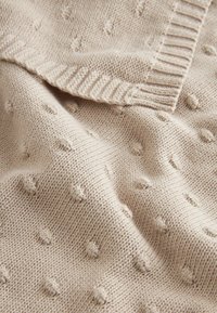 Tessuto di maglia beige con un motivo a pallini testurizzato, caratterizzato da bordi a coste, una texture morbida e una caduta leggera.