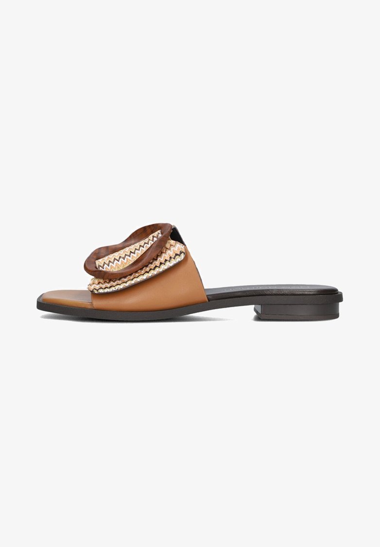 Brown leather slide sandal featuring a rounded top with zigzag trim and a flat heel, showcasing a smooth texture and open design.