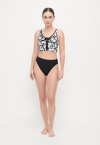 Set bikini bianco e nero con motivo floreale sulla parte superiore e dettaglio a bottone, abbinato a una parte inferiore nera a vita alta. Texture liscia.
