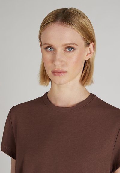 Brązowa koszulka z krótkim rękawem, okrągłym dekoltem i gładką teksturą, charakteryzująca się luźnym krojem oraz prostym, minimalistycznym wzornictwem.