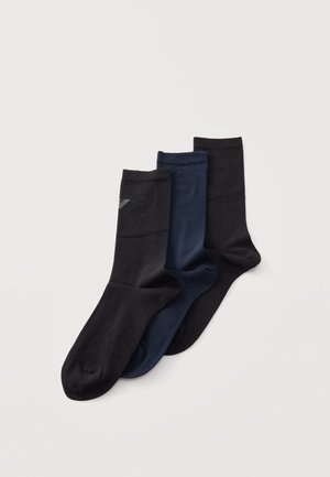 Trois chaussettes mi-mollet, noire, bleu marine et gris foncé, se chevauchent sur un fond clair ; la chaussette noire présente un petit détail rayé.