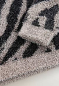 Fuzzy textile featuring a pattern of alternating black and light brown stripes. The surface texture is soft and plush.