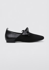 Zapato plano negro con punta afilada, presentado con un upper de ante y un panel de cuero brillante. Un lazo decorativo se encuentra posicionado en la parte frontal.