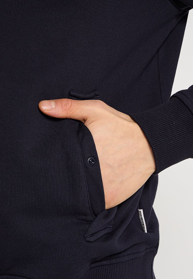 Marinblå sweatshirt med ribbade ärmslut, texturerat tyg och sidoficka. Knapppropp vid fickan ökar funktionaliteten.
