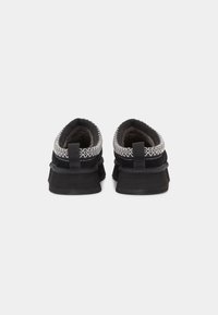 Black shoes with a textured upper, featuring a contrasting silver stitching around the collar and a black, cushioned sole.