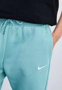 Pantalons de survêtement turquoise clair en tissu doux, dotés d'une taille élastique et d'un logo Nike blanc sur le côté gauche.