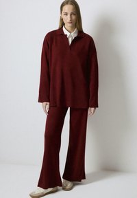 Burgundy two-piece outfit featuring a long-sleeve polo-style top with a collar and flared pants, made of a soft, textured fabric.