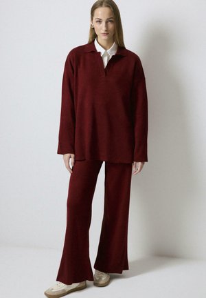 Burgundy two-piece outfit featuring a long-sleeve polo-style top with a collar and flared pants, made of a soft, textured fabric.