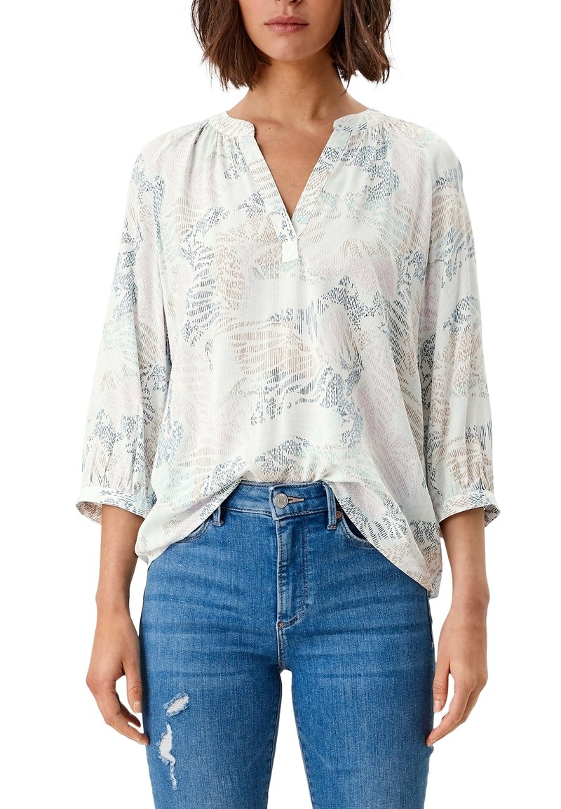 Blouse légère à motif bleu pâle et crème, dotée d'un col en V, de manches 3/4 et d'une coupe décontractée, portée avec un jean en denim bleu.