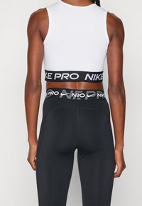 Czarne legginsy Nike Pro w połączeniu z białym sportowym biustonoszem Nike Pro. Cechy obejmują elastyczny pas z logo oraz dopasowany krój.