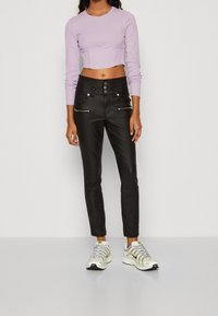 Czarne spodnie z ekoskóry z trzema zamkami błyskawicznymi z przodu, pięcioma guzikami i dopasowanym krojem; w połączeniu z jasnoliliowym topem crop i wielokolorowymi sneakersami.