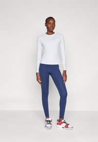Lys blå langermet treningstrøye, tettsittende marineblå leggings og røde og hvite joggesko. Glatt tekstur, sporty design, med logo aksenter.