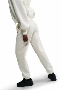 Weiße, eng anliegende Sweatpants mit Bündchen an den Knöcheln, weicher Textur und Seitentaschen, kombiniert mit schwarzen Sportschuhen. Lässiges Sportbekleidungsdesign.