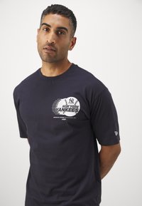 Navy blue cotton T-shirt featuring a stylized white graphic of "New York Yankees" with baseball accents on the front. Short sleeves.