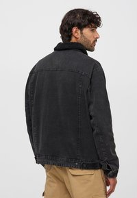 Giubbotto di jeans nero con colletto morbido, dal taglio rilassato, con cuciture in vista e bottoni a pressione ai polsini e all'orlo.