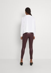 Blusa bianca a maniche lunghe abbinata a leggings bordeaux lucidi. La blusa ha un orlo arrotondato, mentre i leggings presentano una finitura lucida.