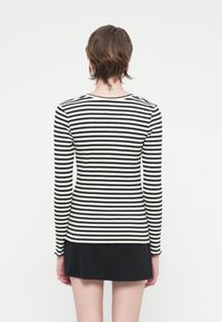 Črno-bela stripe dolg rokav vrh s prilegajočim dizajnom in rebrasto teksturo; okrogla izreza in ravno rob na pasu.
