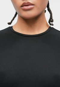 Czarny prążkowany T-shirt z okrągłym dekoltem i krótkimi rękawami, o gładkiej fakturze i dopasowanym kroju. Włosy ułożone w małe warkoczyki.