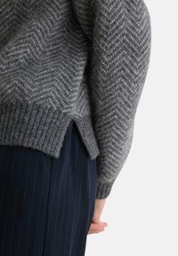 Maglione grigio a maglia con motivo a spina di pesce, orlo a costine e fessure laterali, abbinato a pantaloni blu con righe. 