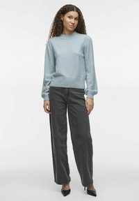 Pull bleu clair avec un col et des poignets côtelés, associé à un jean large taille haute gris foncé et des talons noirs.
