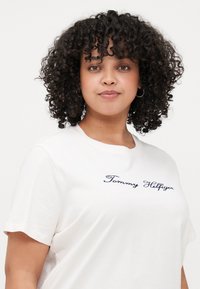Witte t-shirt met korte mouwen en een marineblauw geborduurd "Tommy Hilfiger" logo op de borst. Zachte katoen, ontspannen pasvorm.