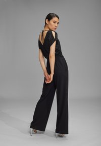 Zwarte pailletten top met korte mouwen, gecombineerd met hoge zwarte wijde broek, met een strikdetail aan de achterkant en zilveren hoge hakken.
