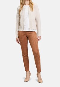 Beige zip-up cardigan over white top, paired with brown suede-like fitted pants and beige pointed heels; smooth texture, tailored fit.