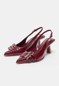 Pantofi cu toc slingback din piele bordeaux, cu vârf ascuțit, două curele argintii cu cataramă și toc bloc, pe un fundal alb.