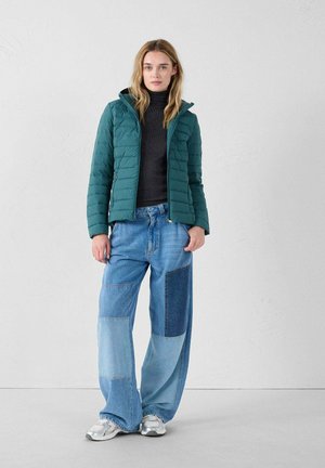 Teal geïsoleerde jas met een capuchon, met een geblokt ontwerp. Gelaagd over een zwarte coltrui en gecombineerd met brede patchwork spijkerbroek.