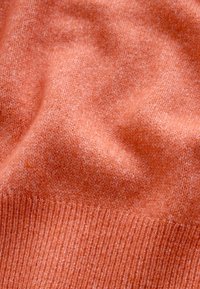 Pehme, tekstuuriga oranž kudumkangas soonikkoes servaga, mis näitab kergeid voltisid ja peent kootud mustrit.