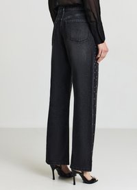 Jeans neri a gamba larga in denim testurizzato. Presentano dettagli con borchie lungo la cucitura laterale e tasche classiche sul retro.