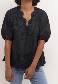 Svart blus med puffärm, med en djup V-ringning och blommig ögla broderi vid bröstet och fållen, med en vågig nederkant.