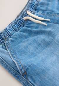 Blue denim pants with an elastic waistband and white drawstrings resting against a light background.