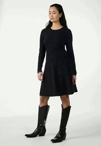 Mustat pitkähihaset mekko, jossa on levenevä hame ja joka on valmistettu pehmeästä kankaasta. Yhdistetty pitkään mustaan nahkasaappaisiin, joissa on sivuvetoketjut.