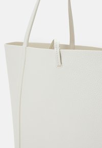 Sac cabas en cuir blanc à finition texturée. Dispose de deux longues anses et d'un design à ouverture supérieure. Lignes épurées et style minimaliste.