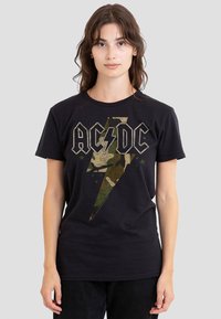 Schwarzes Baumwoll-T-Shirt mit einem großen Camouflage-Blitzgrafik und "AC/DC"-Text darüber, kurzen Ärmeln und klassischer Passform.