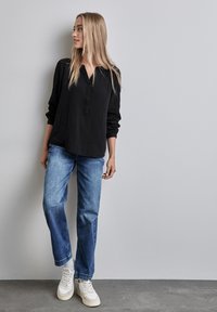 Maglietta nera a maniche lunghe con bottoni davanti, abbinata a jeans azzurri a gamba dritta e sneakers casual bianche. Tessuto morbido.