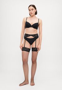 Zwart kanten beha met geschulpte randen, bijpassende kanten kousenband, zwarte slip en zwarte visnetkousen, met ingewikkelde bloemmotieven.