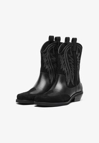 Botas de vaquero negras hechas de cuero y gamuza, con costuras decorativas en un patrón de plumas y tiradores para facilitar su uso.