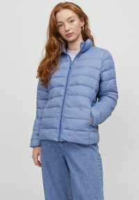 Giacca puffer azzurro chiaro con chiusura a zip, design a righe orizzontali, colletto alto e due tasche laterali. Tessuto morbido e liscio.