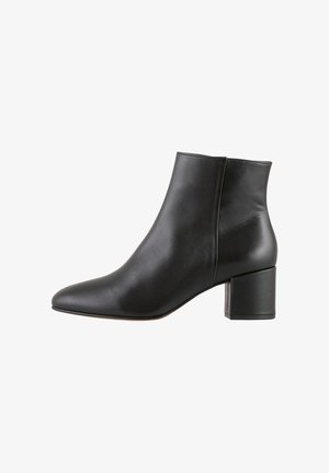 Bottine en cuir noir avec un bout pointu et un talon carré. Texture lisse, éclat subtil et design épuré.