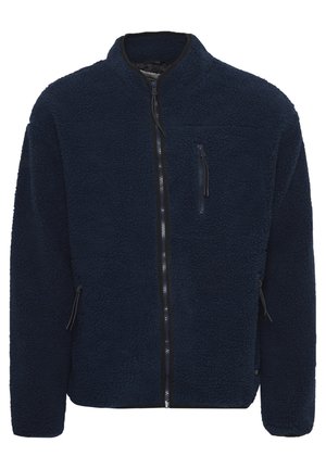 Tengerészeti előnyös polár kabát magas gallérral, teljes elülső cipzárral és két cipzáros oldalsó zsebbel. Texturált anyag, amely puha és meleg tapintású.