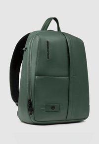 Mochila de cuero verde con un diseño estructurado, que cuenta con un bolsillo frontal, cierre con cremallera y correas acolchadas para los hombros. Textura suave.