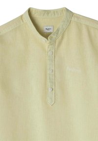 Camicia di cotone giallo chiaro, testurizzata, con colletto alla mandarino, patta con cinque bottoni e logo bianco discreto sul lato sinistro del petto.