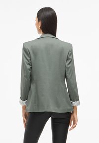 Groene blazer met een getailleerde pasvorm, gelapt revers en gestreepte manchetdetails, met een soepele textuur en mouwen van gemiddelde lengte.