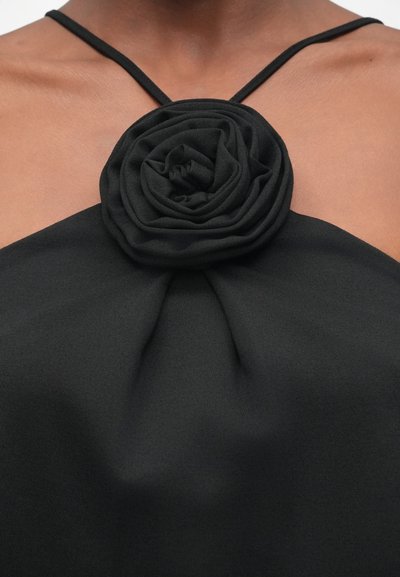 Haut sans manches noir avec un détail de rosette florale au niveau du col. Fabriqué en tissu lisse avec une texture douce et de fines bretelles spaghetti.
