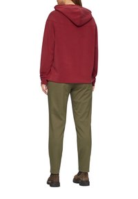 Roter Pullover-Hoodie mit Kängurutasche und einem entspannten Schnitt, kombiniert mit olivgrünen, schmal zulaufenden Hosen. Braune Schuhe runden das Outfit ab.