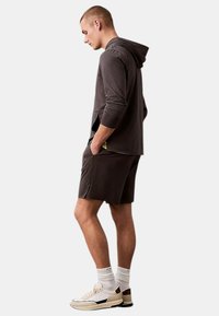 Conjunto deportivo con una sudadera gris oscura y pantalones cortos a juego. La ropa tiene una textura suave y bolsillos funcionales, combinada con zapatillas ligeras.