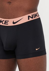 Crne Nike bokserice s ružičastom elastikom na kojoj se nalazi Nike logo u crnoj boji. Glatkasti materijal s minimalnim šavovima i uskim dizajnom.