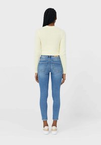 Suéter recortado y difuso de color amarillo claro combinado con jeans azules ajustados. Los jeans tienen bolsillos traseros y un leve desgaste en el dobladillo.